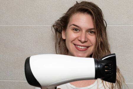 Pretty woman in the bathroom blow drying her hair with electric hair dryerの写真素材