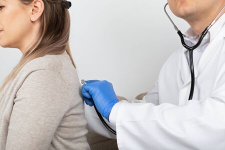 Close up picture of doctor consulting female patient, listening to the lungs while breathingの写真素材