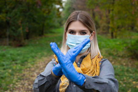 Portrait of caucasian woman with mask and gloves showing stop sign in the park. Autumn colorsの写真素材