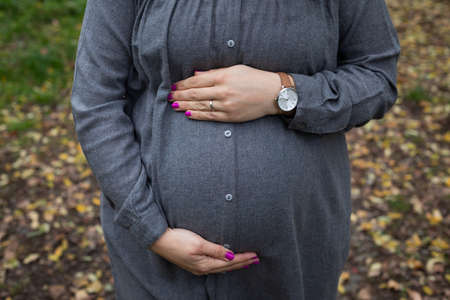 Close up picture of pregnant belly bump in third trimester outdoor in the park at fallの写真素材