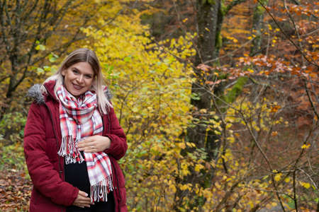 Portrait of cheerful pregnant woman posing outdoor in november, colorful nature in the backgroundの写真素材