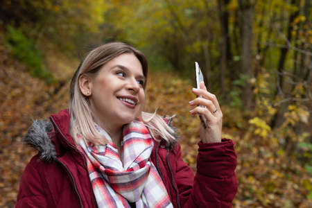 Beautiful young woman making online content with smartphone, colorful autumn background