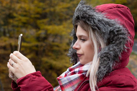 Beautiful young woman making online content with smartphone, colorful autumn background