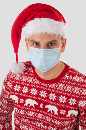 Portrait of young handsome caucasian man wearing Santa's hat, dressed with christmas outfit is posing on isolated with surgical maskの写真素材