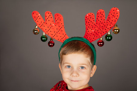 Cute little boy with Christmas outfit and accessories posing in front of grey backgroundの写真素材