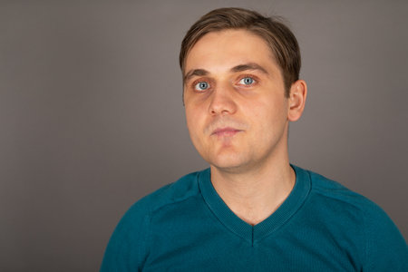 Portrait of a young handsome blond man with blue eyes looking to the camera in front of grey...