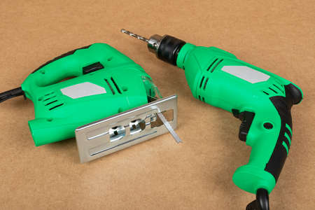 Picture of a green jig sawand a drill on a wooden background