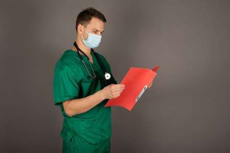 Portrait of young male doctor in green uniform with stethoscope on gray backgroundの写真素材