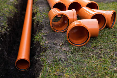 Laying down orange PVC drainage pipes into the groundの写真素材