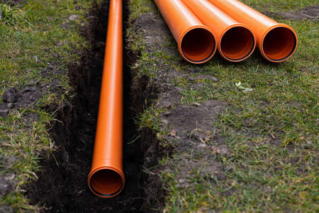 Laying down orange PVC drainage pipes into the groundの写真素材
