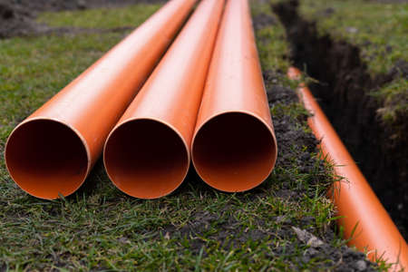 Laying down orange PVC drainage pipes into the ground