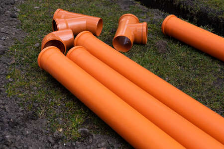 Laying down orange PVC drainage pipes into the groundの写真素材