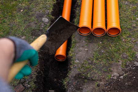 Laying down orange PVC drainage pipes into the groundの写真素材
