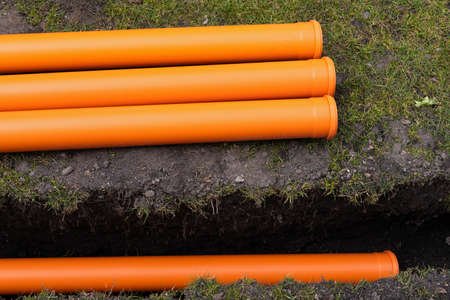 Laying down orange PVC drainage pipes into the groundの写真素材