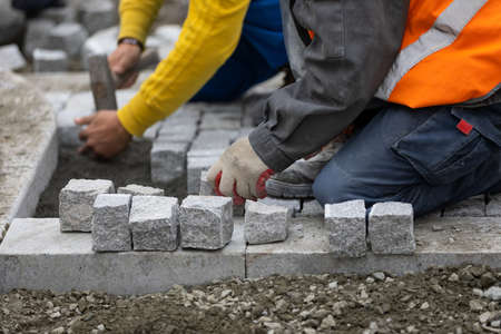 Man in uniform laying  cobblestone sidewalk  on the construction siteの写真素材