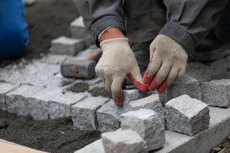 Man in uniform laying  cobblestone sidewalk  on the construction siteの写真素材