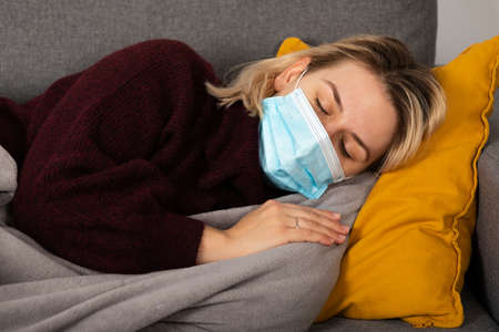 Young woman with coronavirus is having headache and fever, lying on the sofa wrapped in a balnketの写真素材