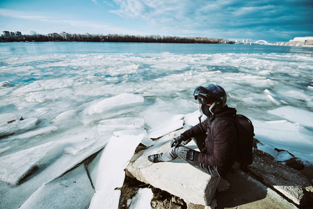 A young motorcycle enthusiast enjoying a beautiful view of a frozen river after his first winter bike rideの写真素材