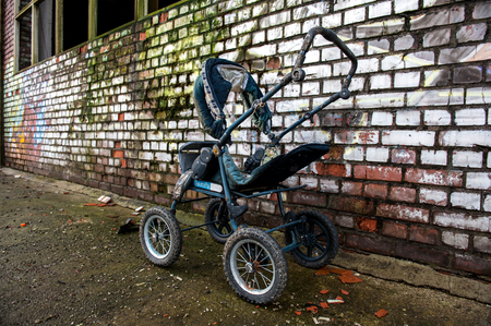 Abandoned blue stroller in front of a painted brick wallの写真素材