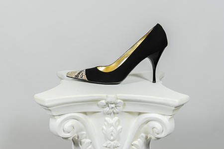 Elegant female high-heeled black leather shoe with snake skin application on greek columnの写真素材