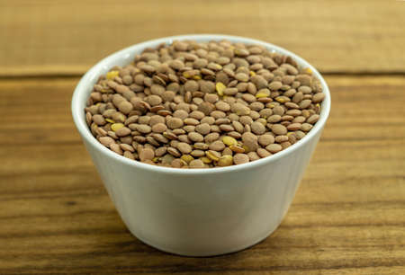 White ceramic bowl of green uncooked lentils isolated on wood in perspective.の写真素材