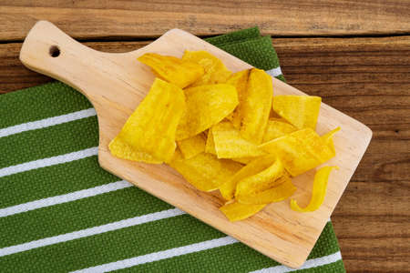 Crispy Banana Chips. Fried or baked sliced banana. Top view of typical traditional dish of Latin American gastronomy called Chifles or fried tostones on a wooden table. Roasted banana. Snack