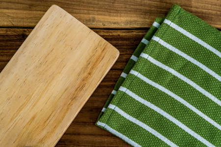 Top view of a wooden chopping board and a green kitchen tablecloth or napkin on a rustic wooden table. Rustic. Restaurant. Serviette. Dishware. Handmade.の写真素材
