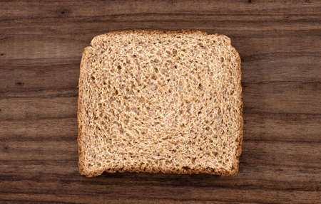 A slice of brown bread with cereals isolated on a wooden tableの写真素材
