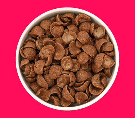 Top view of bowl with sweet chocolate cereal flakes for breakfast on red backgroundの写真素材