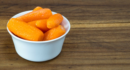 Small baby carrots in soup plates on cutting board. Bowl with fresh carrots on table.の写真素材