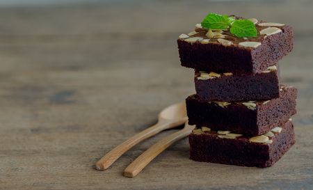 Piece of stack homemade dark chocolate brownies topping with almonds slices and mint on wood table.Bitter,sweet and fudge.Brownie is one type of chocolate cake. Natural tone.の写真素材