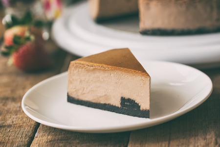 Homemade chocolate cheesecake on rustic wood table.Baked chocolate cheesecake on plate.Brownie cheesecake for coffee break or tea time in cafe.Triangle slice piece of chocolate cake in dramatic style.の写真素材