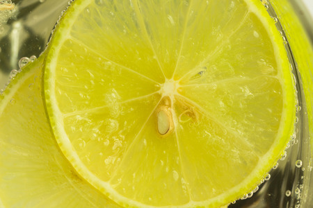 Close up concept on piece of lemon or lime in lemonade for wallpaper or background. Half-circle of lemon or lime in sparkling water (soda) in natural tone. Water bubble and half-circle lemon or lime.の写真素材