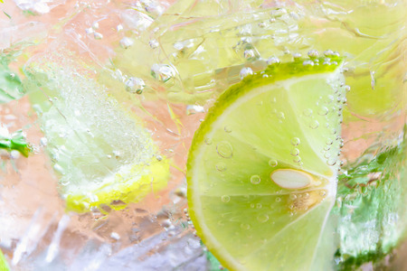 Close up concept on piece of lemon or lime in lemonade for wallpaper or background. Half-circle of lemon or lime in sparkling water (soda) in natural tone. Water bubble and half-circle lemon or lime.の写真素材