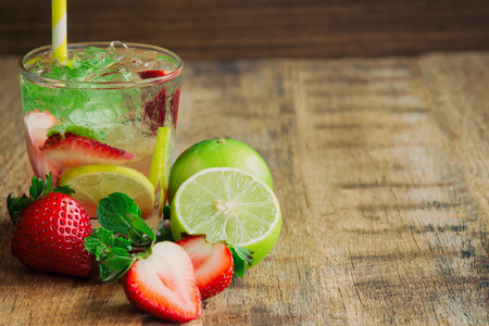 Strawberry lemon lime mojito in clear glass on rustic wood table. Homemade beverage strawberry soda ingredients with strawberry, lemon or lime and mint leaf. Homemade infused water with copy space.の写真素材