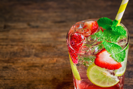 Strawberry lemon lime mojito in clear glass on rustic wood table. Homemade beverage strawberry soda ingredients with strawberry, lemon or lime and mint leaf. Homemade infused water close up concept.の写真素材
