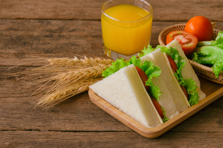 Piece of sandwich ham cheese with lettuce and tomato on wood plate. Homemade sandwich served with orange juice for breakfast or lunch. Delicious ham and cheese sandwich ready to served on wood table.の写真素材