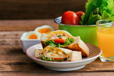 Pocket sandwich for breakfast or lunch. Homemade sandwich with hard boiled eggs and mayonnaise decorated by lettuce and tomato. Baked sandwich on lovely plate serve with orange juice on wood table.の写真素材