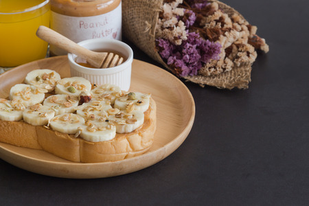 Banana peanut butter toast sandwich on wood plate with honey. Homemade open sandwich spread with peanut butter on top with banana slice and granola. Delicious healthy sandwich for breakfast or lunch.の写真素材