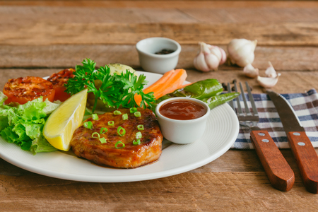 Barbecue pork steak on white plate served with barbecue sauce and vegetables. Pork steak for lunch or dinner on wood table. Moist and soft homemade pork barbecue served with mash potato and vegetable.の写真素材