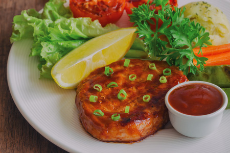 Barbecue pork steak on white plate served with barbecue sauce and vegetables. Pork steak for lunch or dinner on wood table. Moist and soft homemade pork barbecue served with mash potato and vegetable.の写真素材