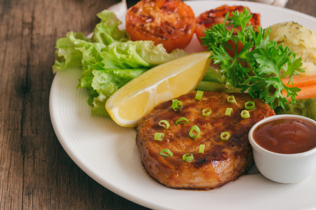 Barbecue pork steak on white plate served with barbecue sauce and vegetables. Pork steak for lunch or dinner on wood table. Moist and soft homemade pork barbecue served with mash potato and vegetable.の写真素材