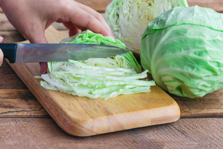 Chopped fresh cabbage on wood cutting board for food. Woman use knife kitchen cutting cabbage prepare for cooking. Cut or sliced fresh cabbage to shredded for coleslaw salad or other food.の写真素材