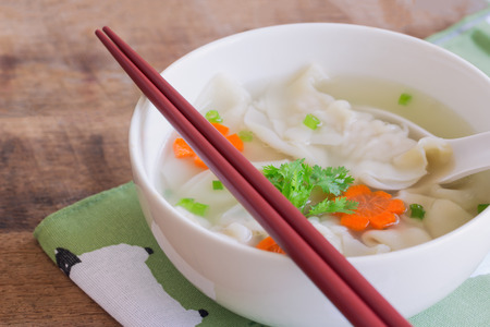 Homemade minced pork wonton soup in white bowl on napkin put on wood table. Delicious wonton in clear soup for breakfast or lunch or dinner. Wonton or dumpling is always popular Chinese food.の写真素材