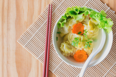 Homemade minced pork and shrimp wonton soup in white bowl on wood table in top view flat lay.Delicious wonton in clear soup for breakfast or lunch or dinner.Wonton or dumpling is popular Chinese food.の写真素材