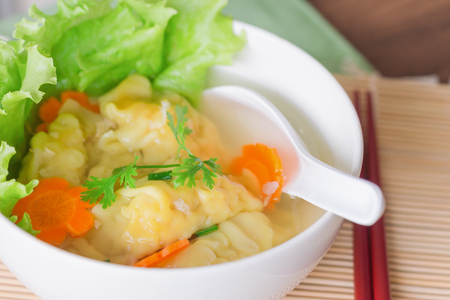 Close up minced pork and shrimp wonton soup or dumpling in white bowl on wood table. Homemade delicious dumpling soup for breakfast or lunch or dinner. Wonton or dumpling soup is popular Chinese food.の写真素材