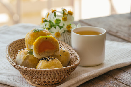 Delicious Chinese pastry or moon cake filled with mung bean paste and salted egg yolk on wood basket served with tea on wood table in side view, close up with copy space. Homemade bakery concept.の写真素材