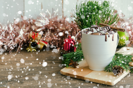 Hot chocolate in white cup topping with marshmallow and dark chocolate sauce on wood table in side view, copy space with Christmas theme and snowfall background. Concept to present Xmas drink.の写真素材