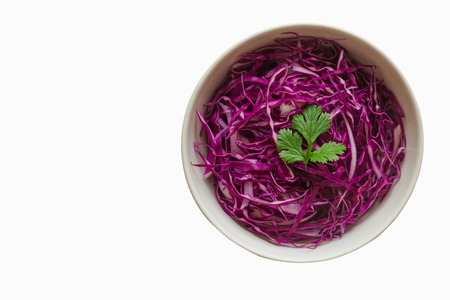 White isolated background with clipping paths sliced fresh purple cabbage in white bowl in top view flat lay. Prepare vegetable for cooking cabbage salad or coleslaw. Homemade food concept.の写真素材