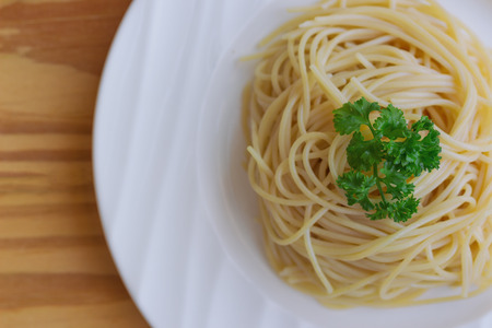 Boiled spaghetti with al dente level. Cooked pasta prepared for cooking on white plate, close up in top view flat lay view with copy space on wood table. Homemade Italian traditional food concept.の写真素材